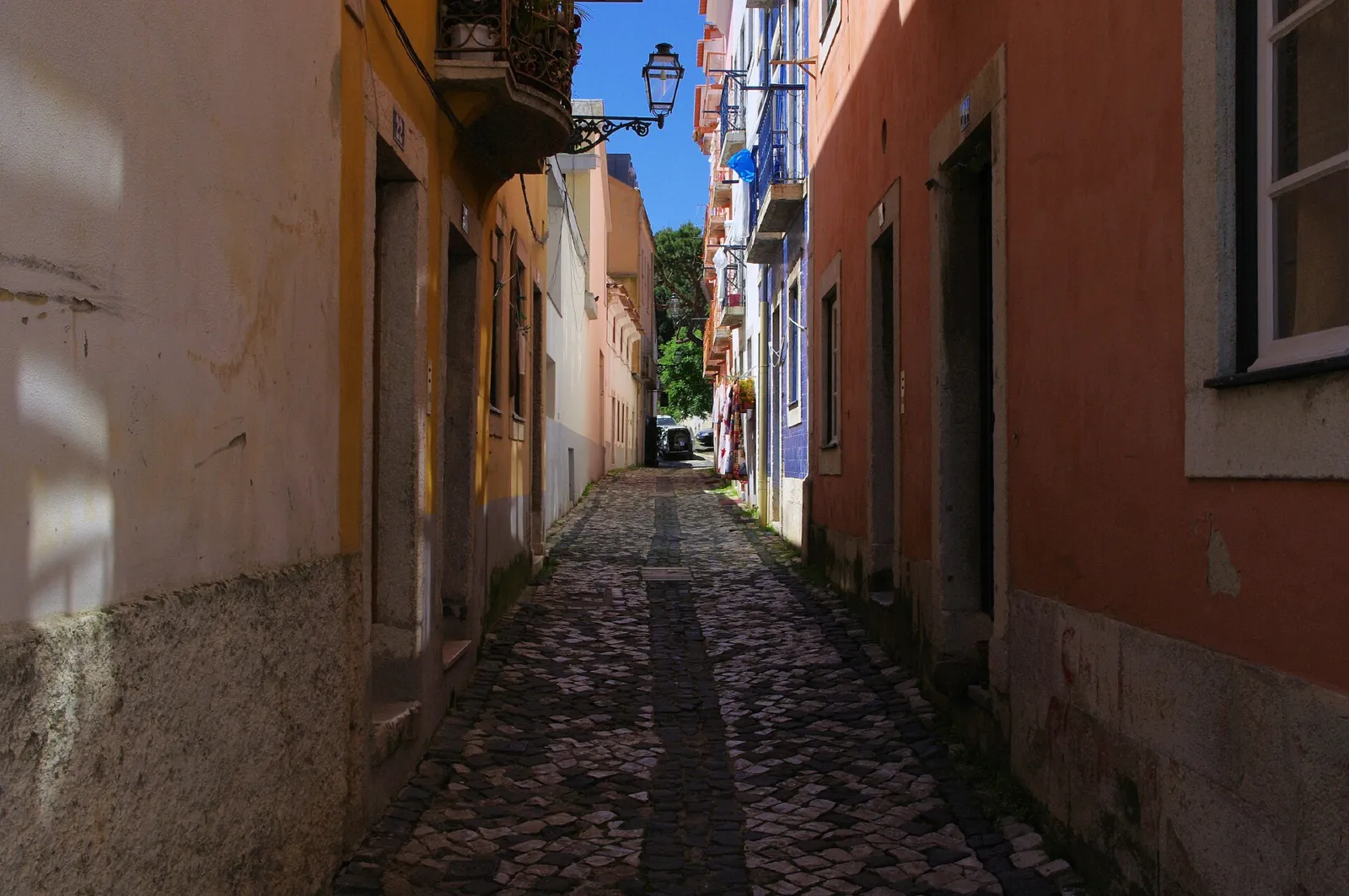 Callejón empedrado y estrecho del barrio de Alfama con fachadas de colores cálidos
