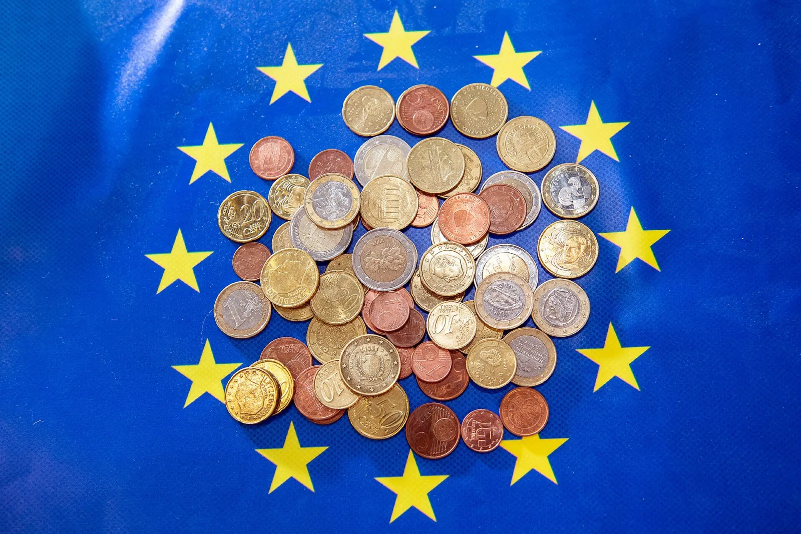 Montón de monedas de euro sobre una bandera azul de la Unión Europea con estrellas amarillas