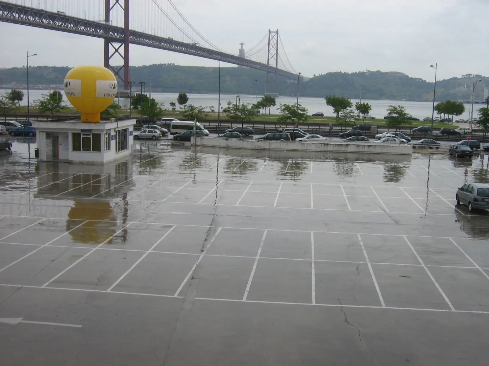 Explanada de Lisboa mojada por la lluvia con el puente 25 de Abril entre nubes grises