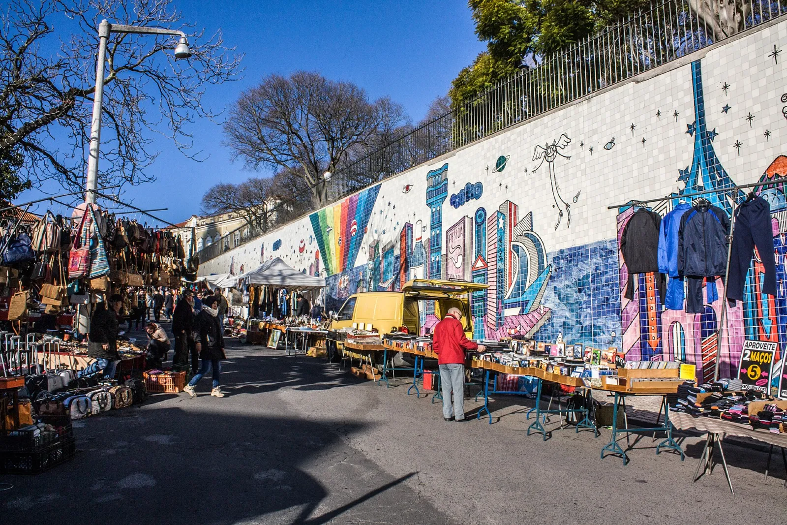 Puestos de la Feira da Ladra junto a un muro cubierto de azulejos y grafitis en Lisboa