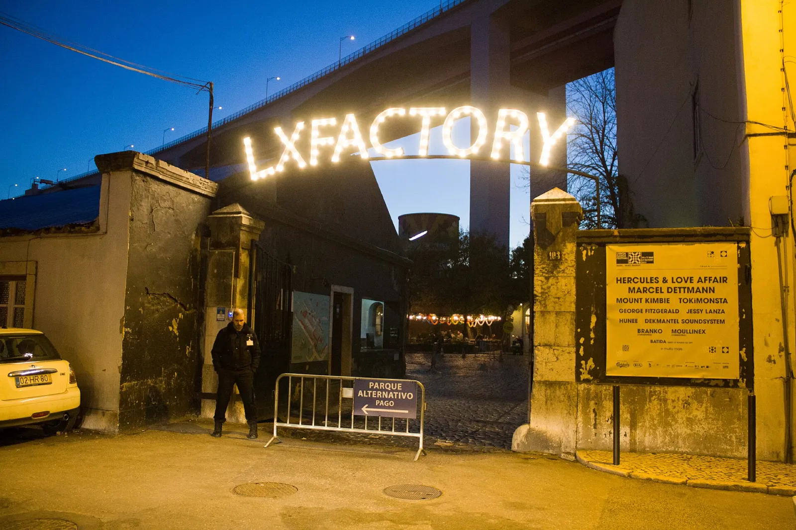 Entrada nocturna iluminada con el rótulo luminoso de LX Factory bajo el puente de Lisboa