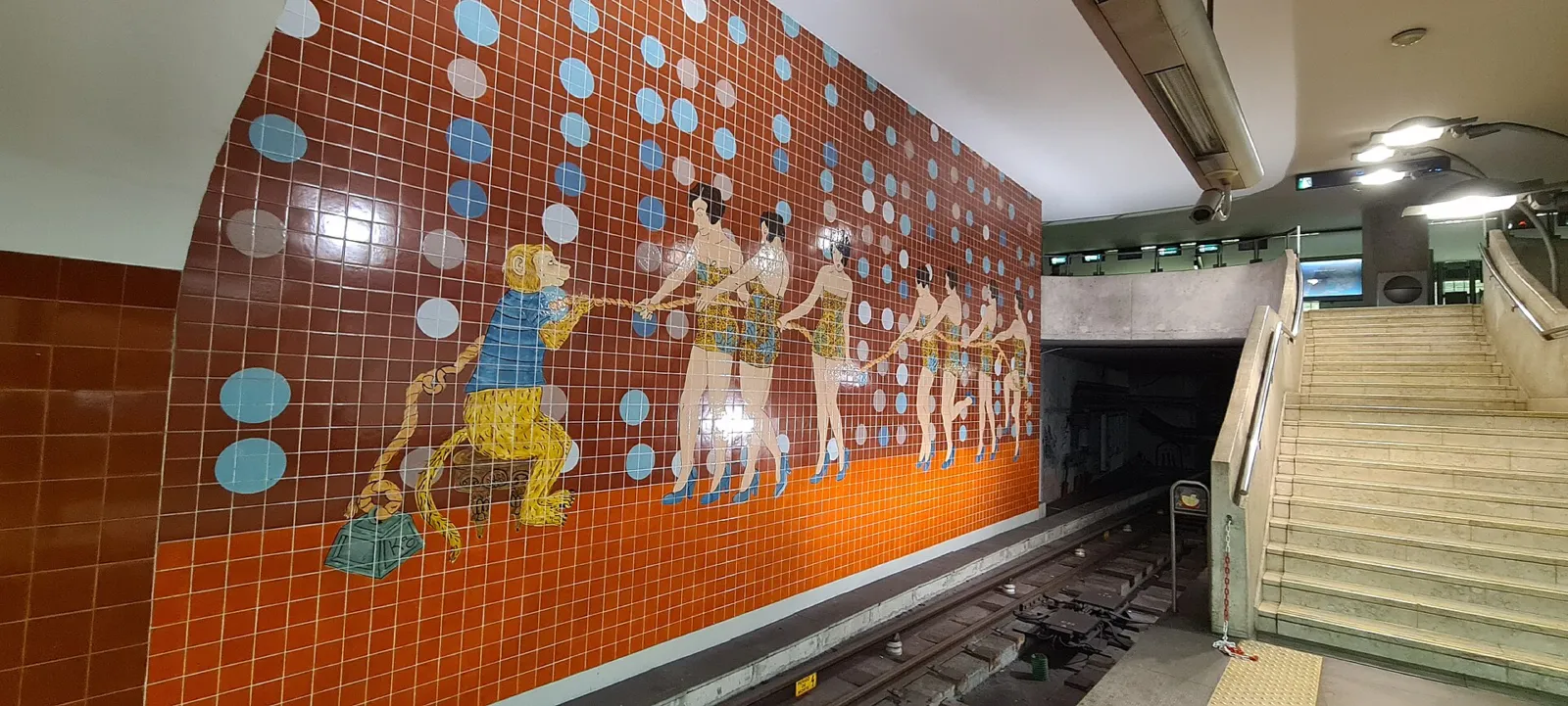 Estación del metro de Lisboa con un mural de azulejos coloridos y escaleras al fondo