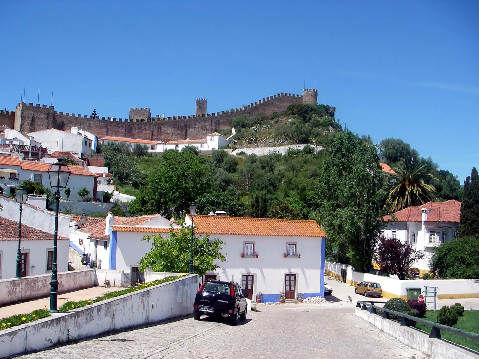 Murallas medievales y casas blancas de Óbidos bajo un cielo azul, con el castillo al fondo