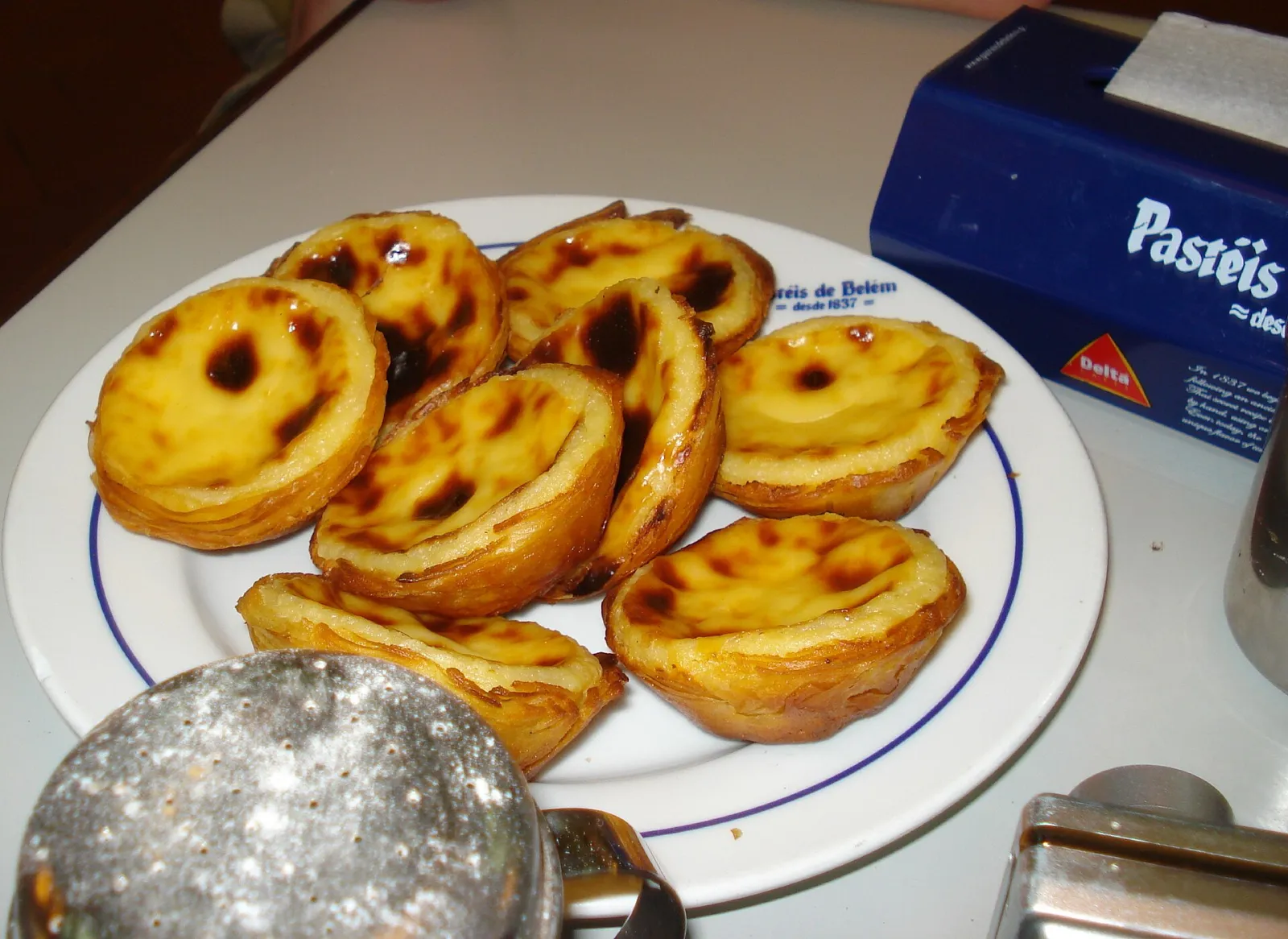 Plato de pastéis de nata recién hechos junto a una caja de Pastéis de Belém