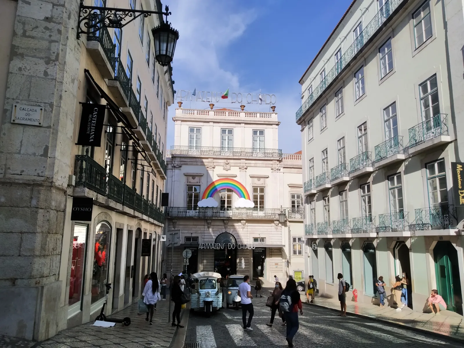 Calle empinada del Chiado en Lisboa con edificios clásicos y transeúntes con ropa cómoda de verano