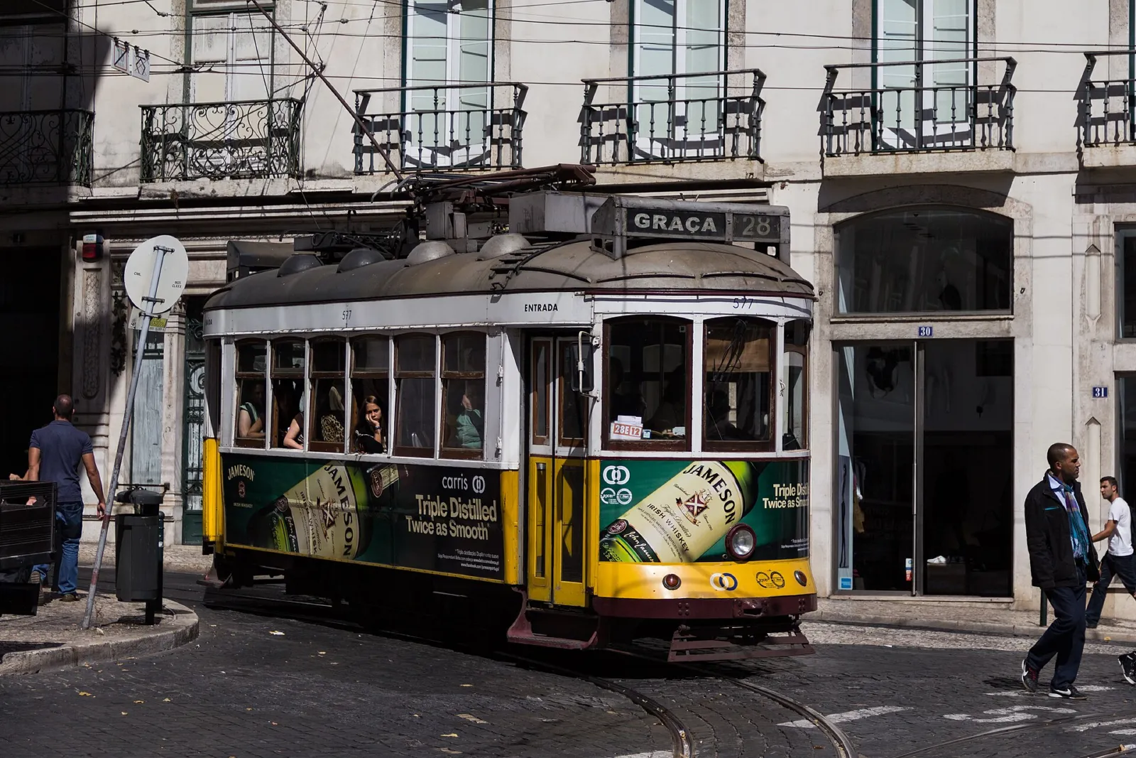 Tranvía 28 amarillo con destino Graça girando por una calle empedrada de Lisboa