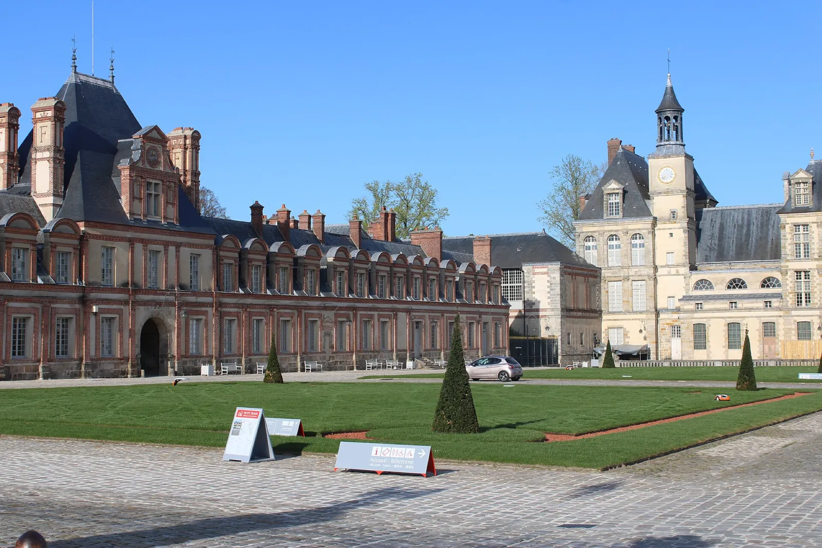 Cour du Cheval Blanc del castillo de Fontainebleau con sus alas de ladrillo y piedra y el césped