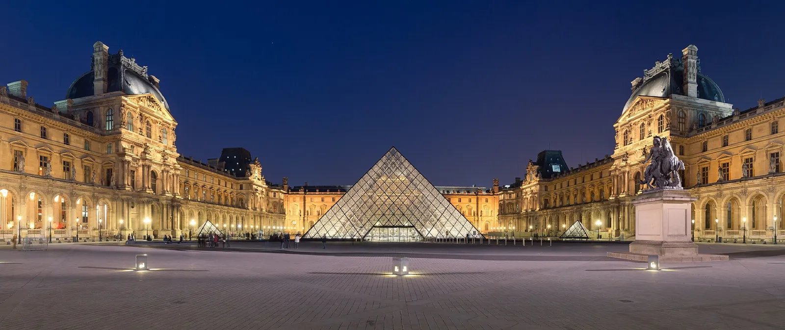 Palacio del Louvre y su pirámide de cristal iluminados al anochecer en la Cour Napoléon
