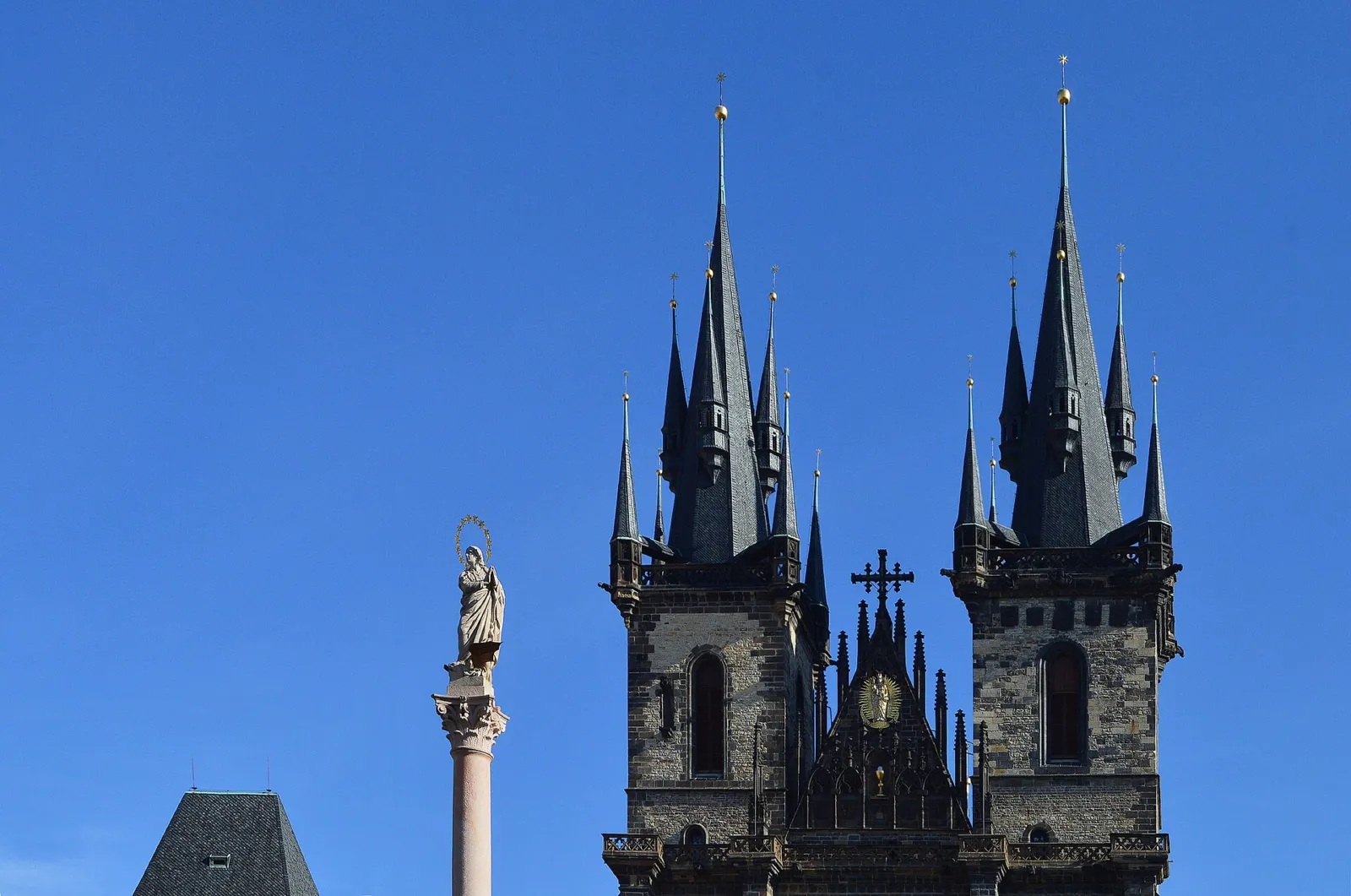 Torres góticas de la iglesia de Nuestra Señora de Týn y la columna mariana bajo un cielo azul